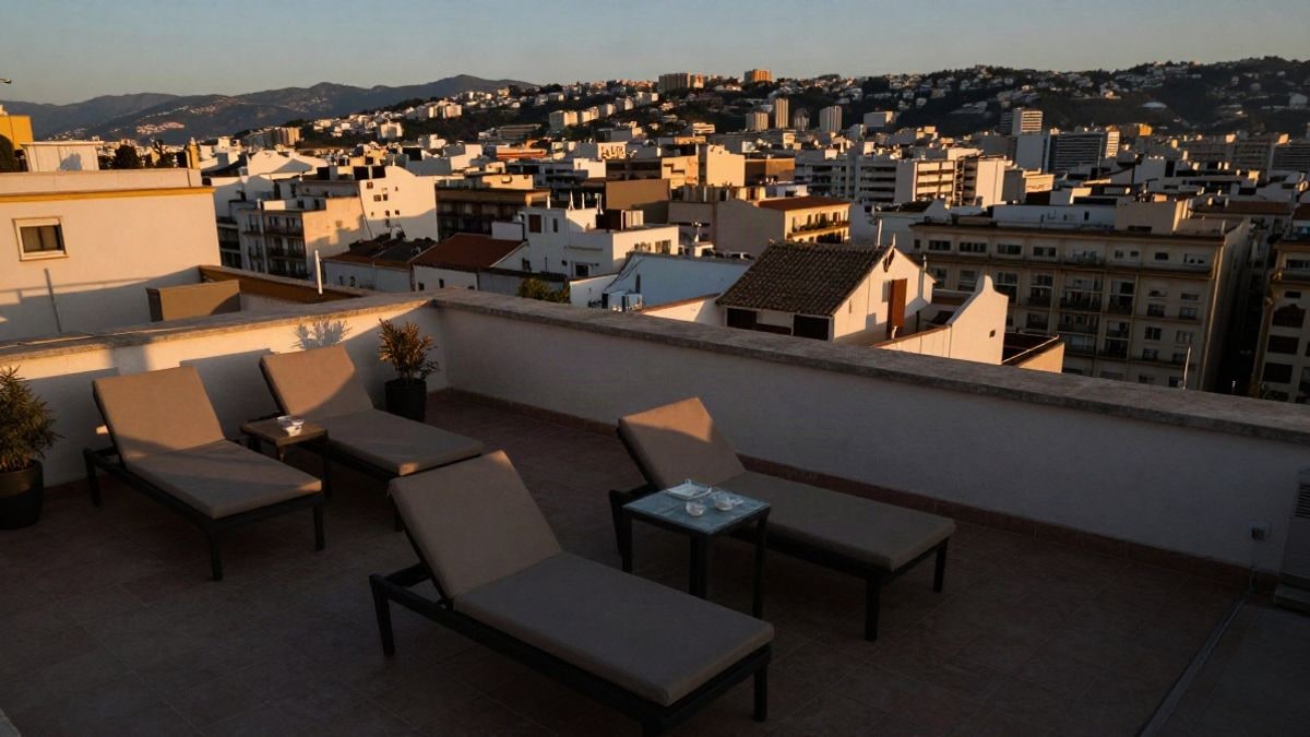 Imagen ilustrativa: terraza de hotel con tumbonas vacías y vistas a una ciudad mediterránea al atardecer