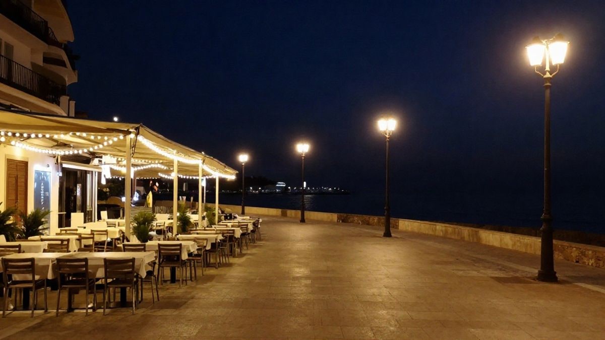 Imagen ilustrativa: paseo marítimo mediterráneo de noche con luces cálidas y terrazas vacías