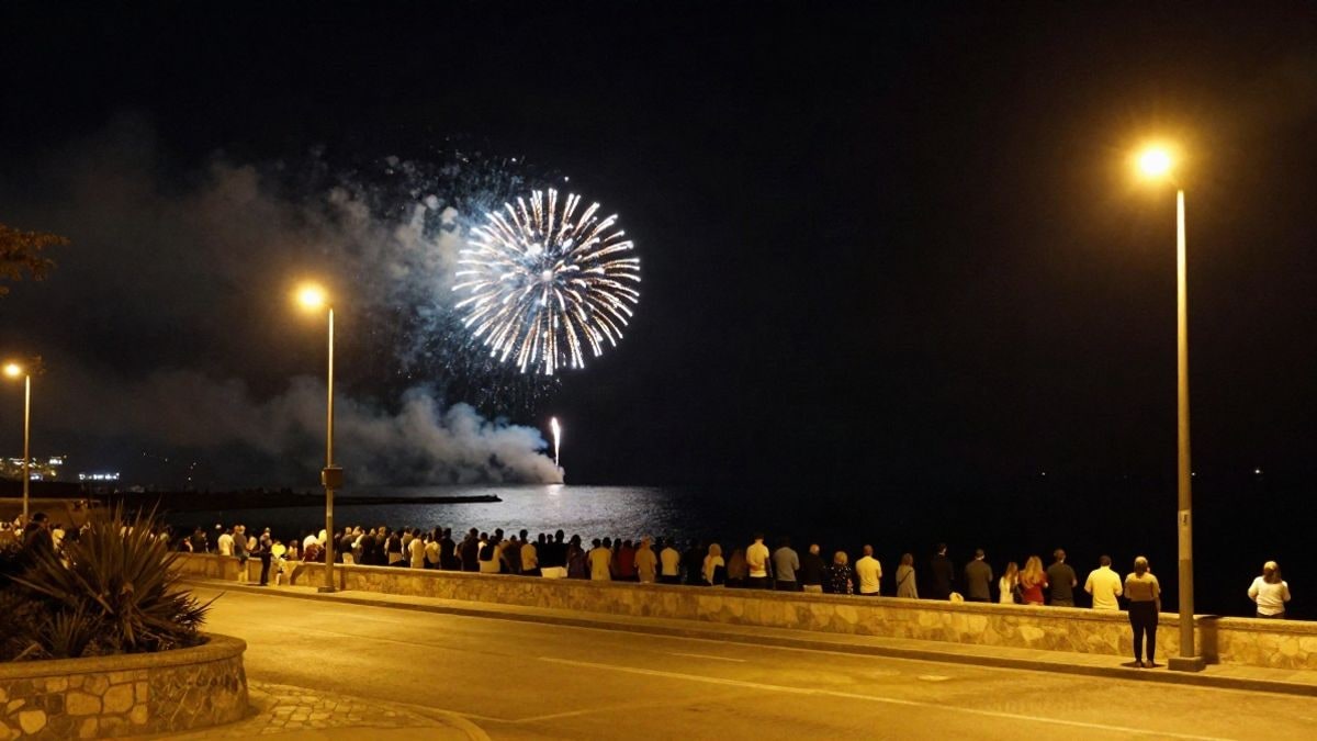 Imagen ilustrativa: mirador nocturno junto al mar iluminado por focos y farolas, con fuegos artificiales sobre el agua