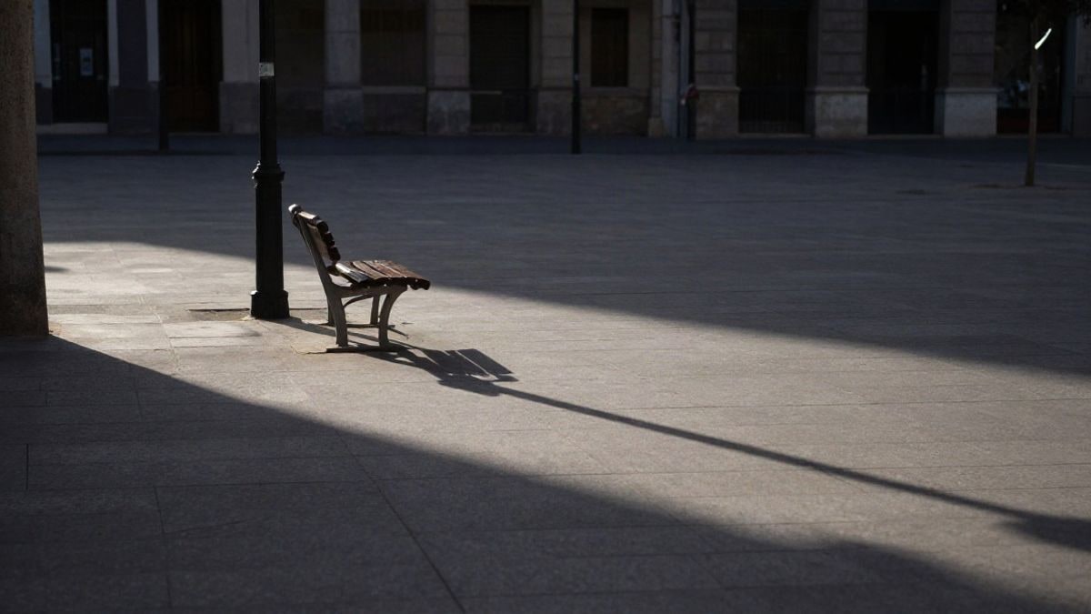 Imagen ilustrativa: una plaza urbana vacía al atardecer con un banco solitario bajo una farola y largas sombras en el pavimento