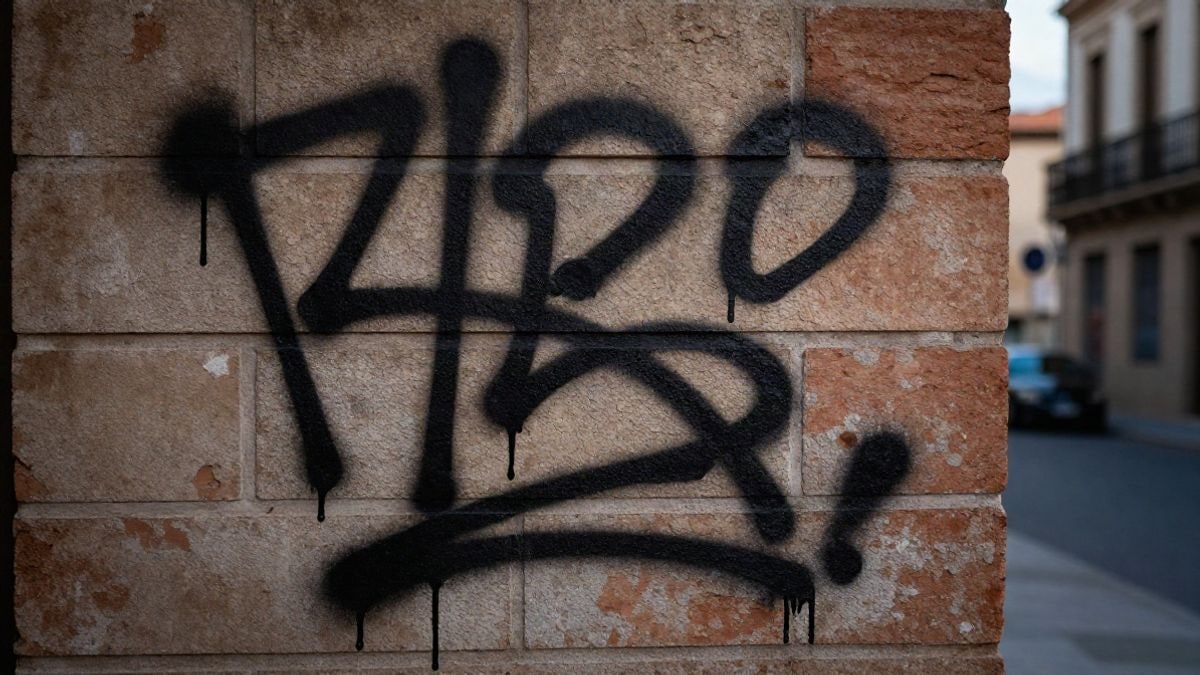 Imagen ilustrativa: pared de ladrillo con pintadas abstractas en spray negro al amanecer.