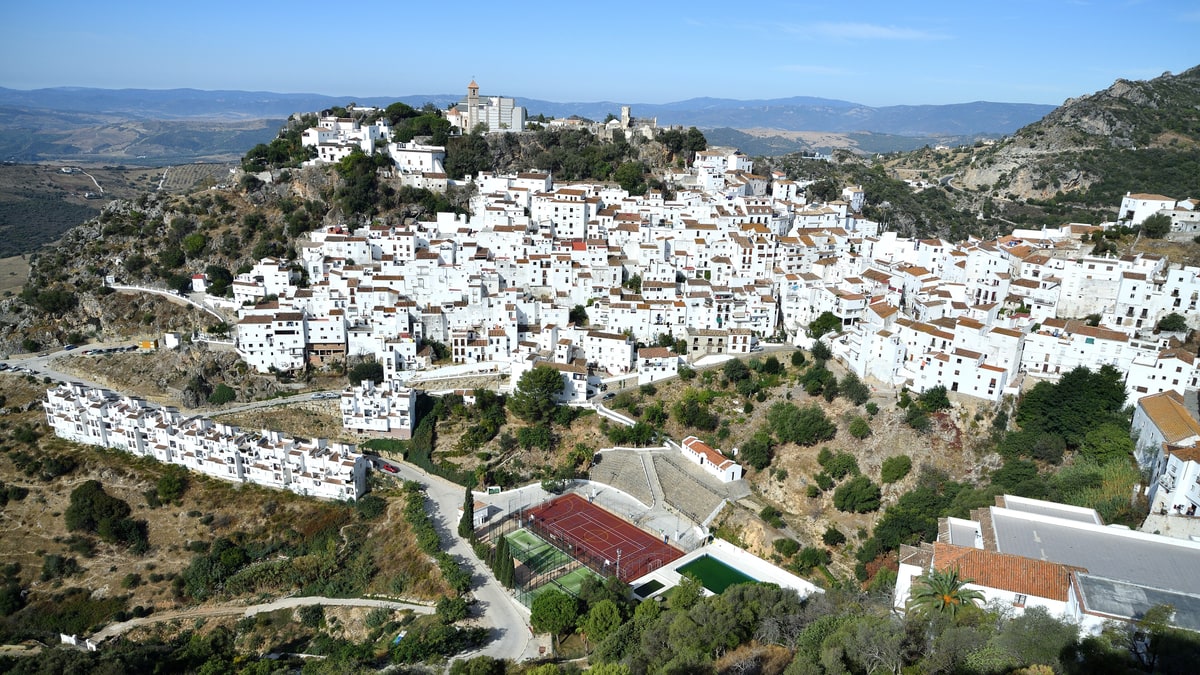 Panoramic view of the white town of Casares perched on the hill, with its church and fields in the background.