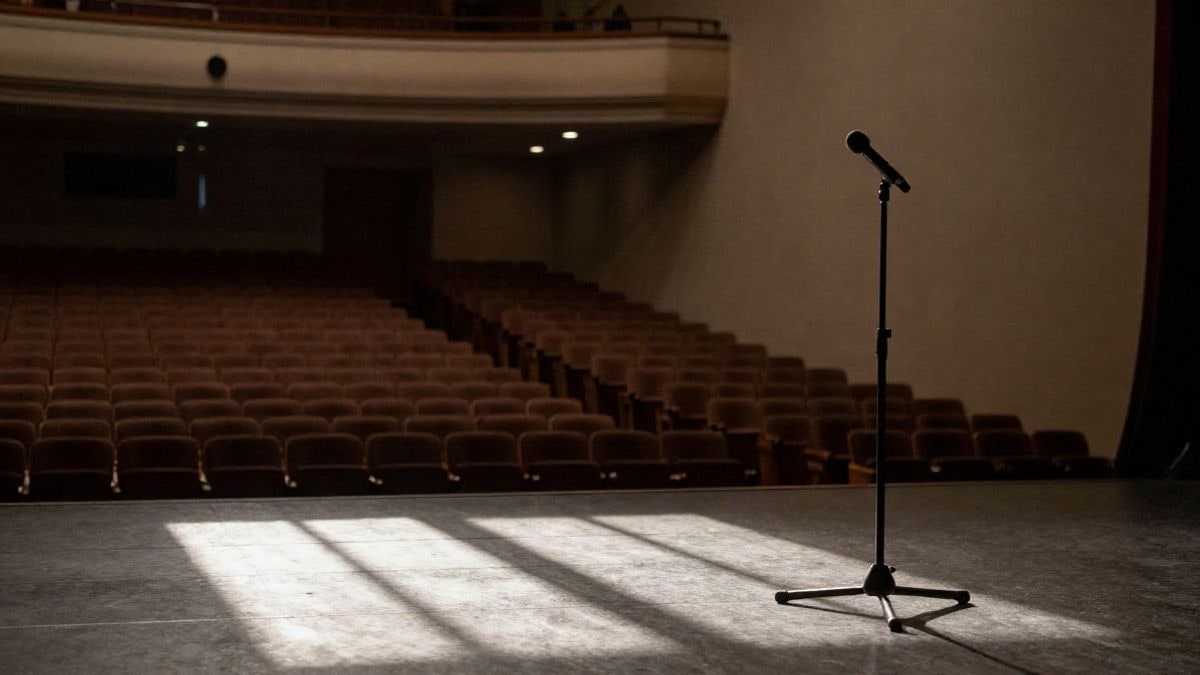 Illustrative image: interior of a theatre with empty seats and a microphone on stage