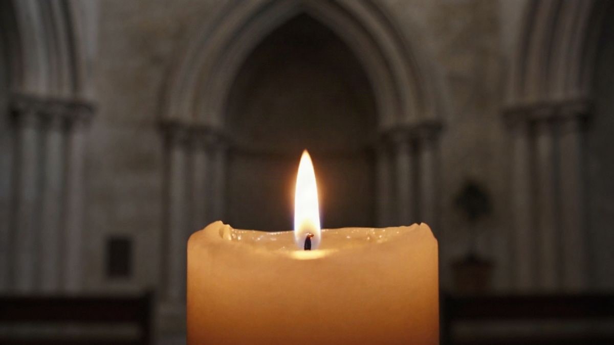 Imagen ilustrativa: primer plano de una vela encendida en el interior de una iglesia de piedra