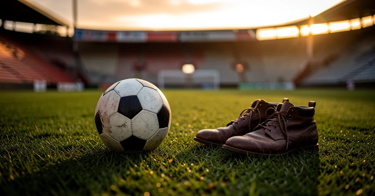 Balón de fútbol y botas sobre el césped de un estadio vacío al atardecer