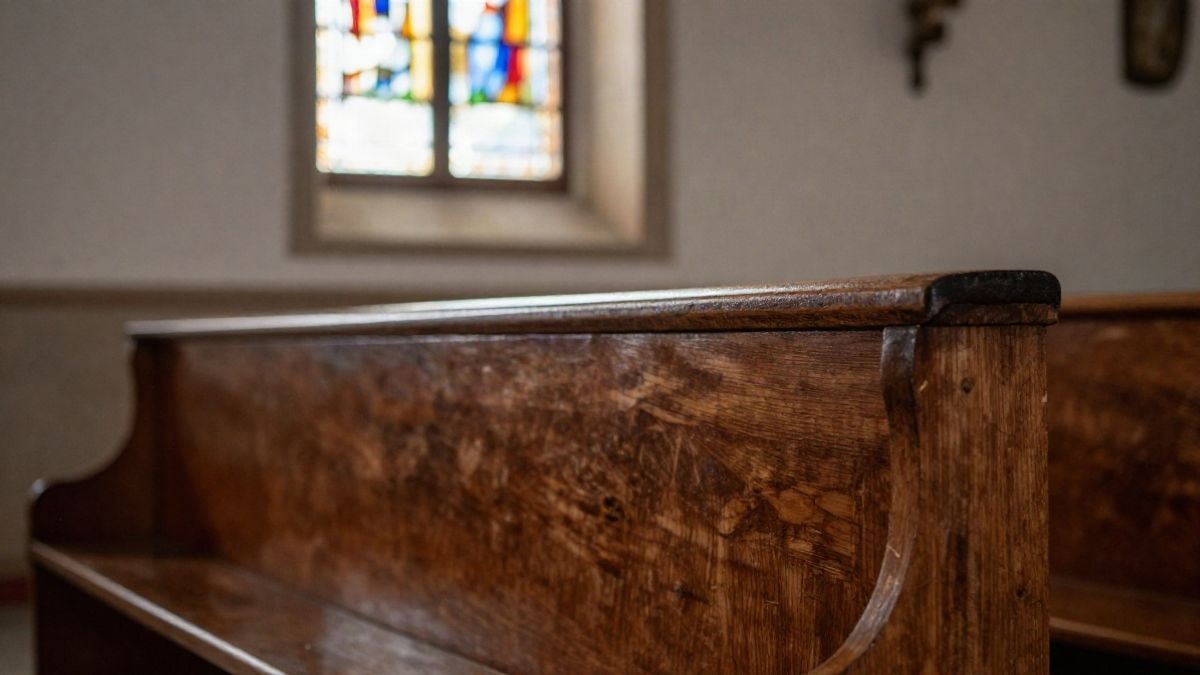 Illustrative image: detail of a wooden church pew with stained glass light in the background