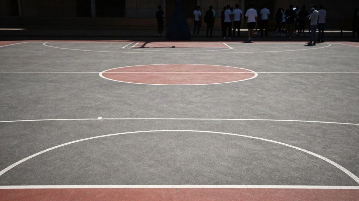 Imagen ilustrativa: una cancha de baloncesto renovada con un balón en el suelo y una canasta al fondo, iluminada por luz lateral.