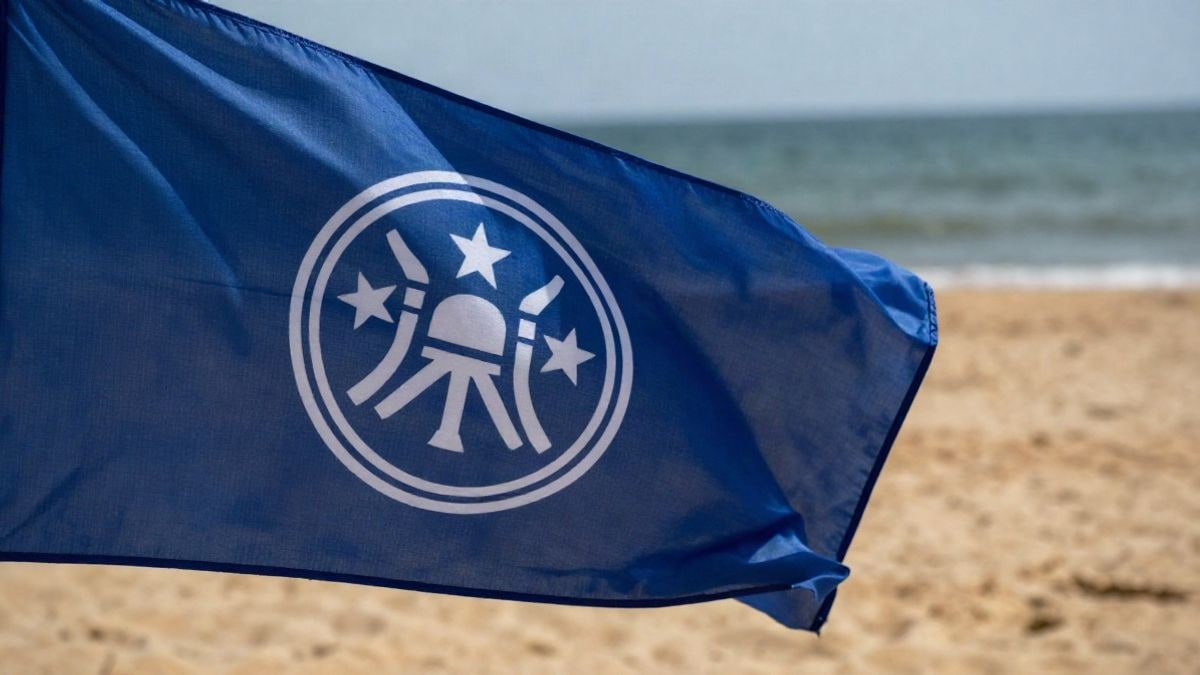 Imagen ilustrativa: primer plano de una bandera azul de certificación ondeando en una playa