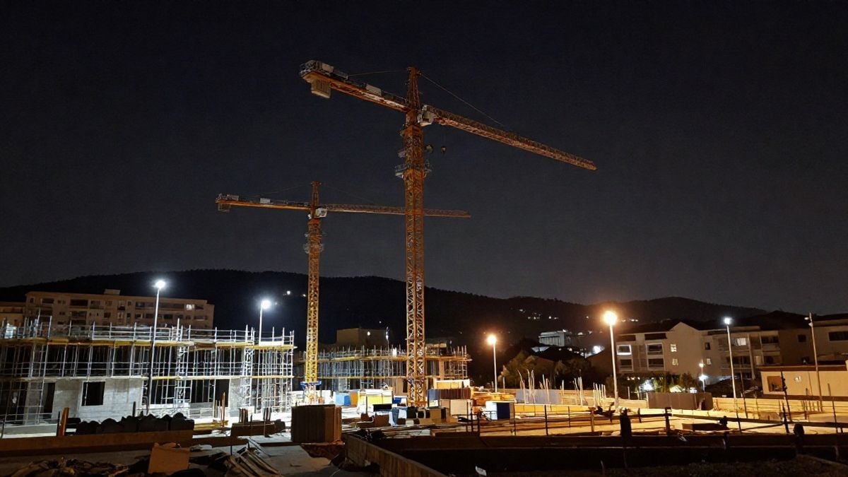 Imagen ilustrativa: grúas y bloques de viviendas en construcción iluminados por focos durante la noche