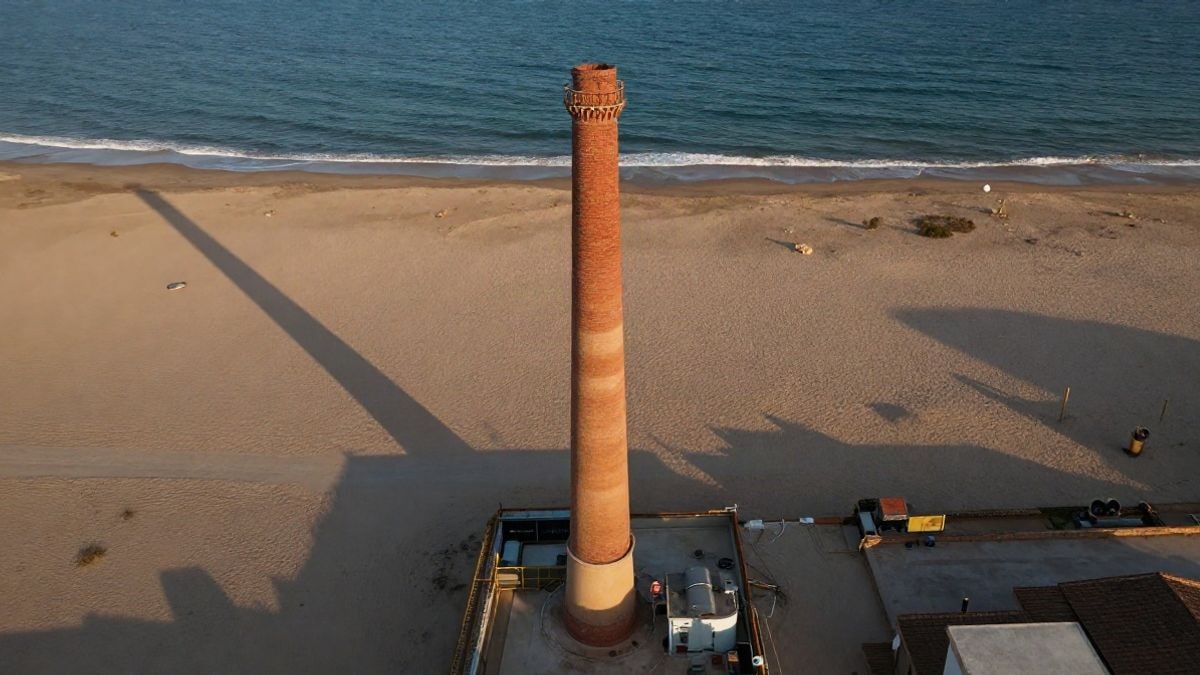 Imagen ilustrativa: vista cenital de una chimenea industrial de ladrillo en una playa al atardecer
