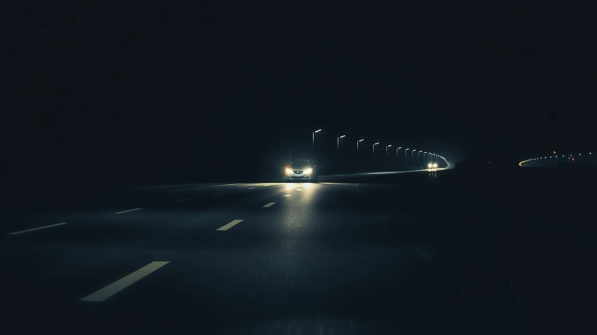 Imagen ilustrativa: autovía nocturna con un vehículo averiado en el arcén y luces de emergencia, vista a ras de asfalto.