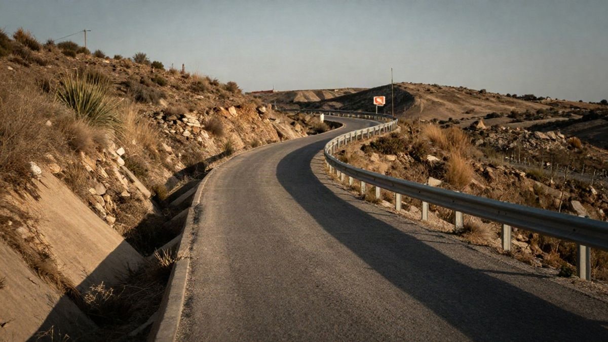 Imagen ilustrativa: carretera rural estrecha con cunetas de hormigón y barreras metálicas al atardecer
