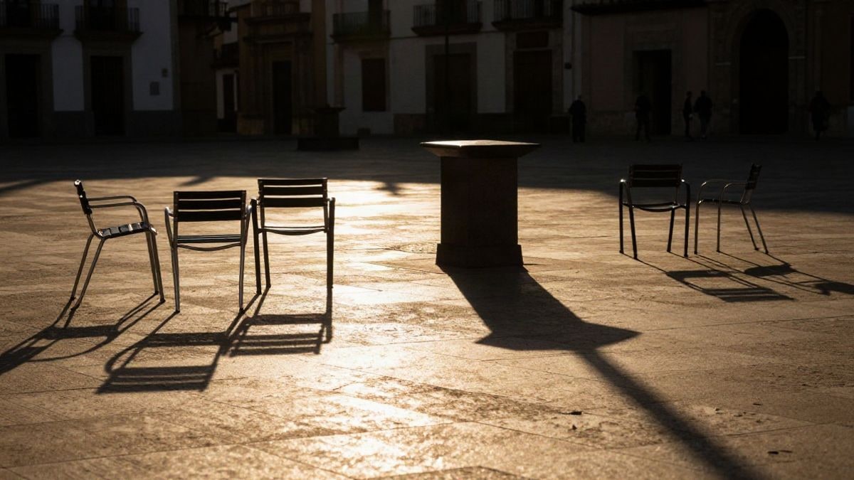 Illustrative image: backlight at sunset with silhouettes and long shadows of a cultural square with empty chairs