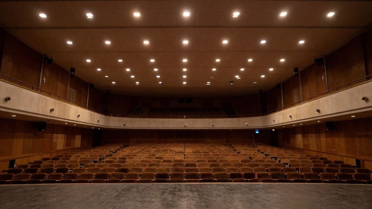 Imagen ilustrativa: escenario de un auditorio vacío con sillas y focos cálidos desde un ángulo bajo