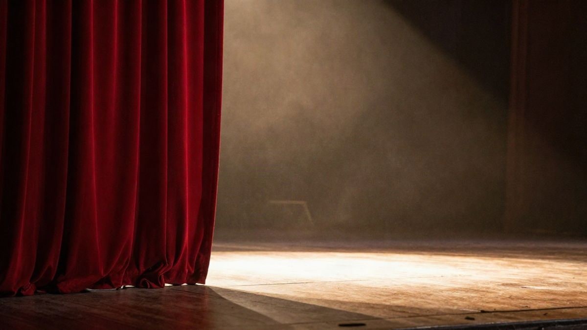 Illustrative image: an empty theatre stage with the red curtain slightly open and a warm light spotlight on the wooden floor.