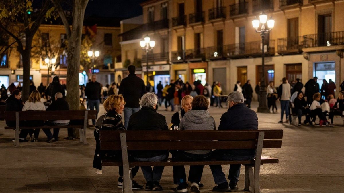 Illustrative image: Spanish public square at night with artificial light and elderly neighbours talking with their backs turned