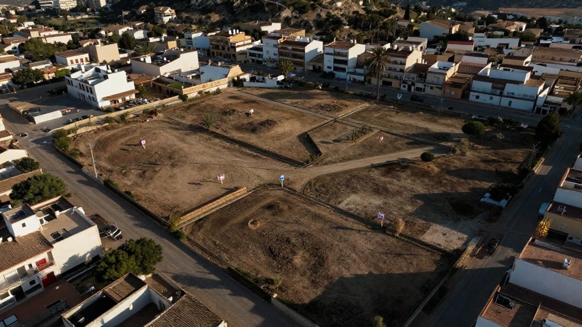 Imagen ilustrativa: vista aérea de parcelas de suelo municipal vacías en una zona urbana costera, con algunas señales de futura construcción.