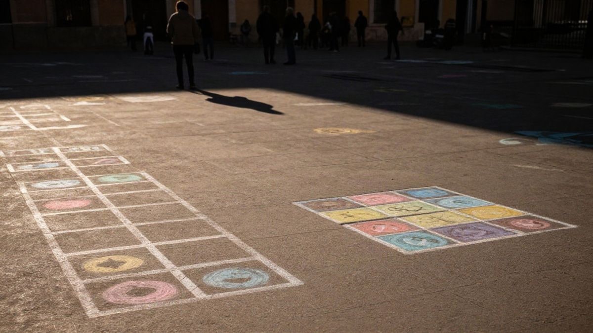 Imagen ilustrativa: dibujos de rayuela y tres en raya en el suelo de una plaza con comba y luz de atardecer