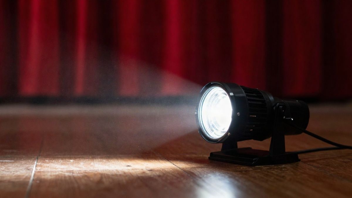 Illustrative image: close-up of a lit stage spotlight on a dark wooden floor