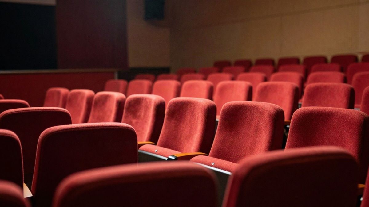 Imagen ilustrativa: butacas rojas de un teatro vacío vistas de lado con luz cálida