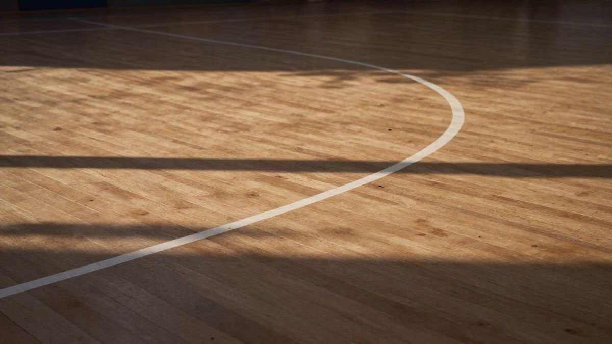 Imagen ilustrativa: detalle de un suelo de madera de pista de baloncesto con líneas blancas, iluminado por luz lateral de atardecer