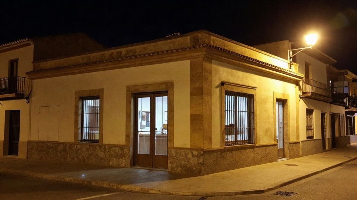 Illustrative image: facade of a municipal office lit by streetlights and interior lights in a coastal town at dusk