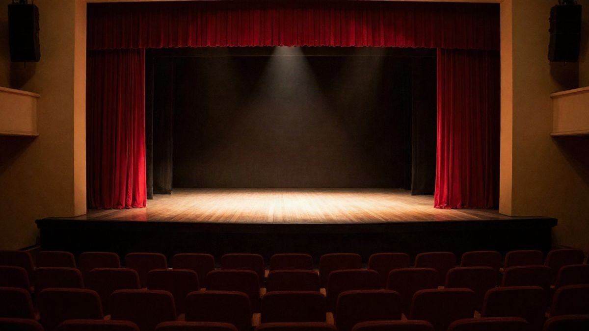Imagen ilustrativa: un escenario teatral vacío con cortinas rojas y un foco de luz central, con butacas en primer plano.