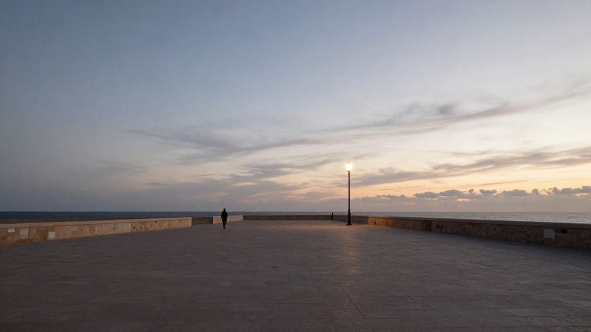 Imagen ilustrativa: paseo marítimo de una localidad costera al atardecer con una farola encendida y una figura lejana