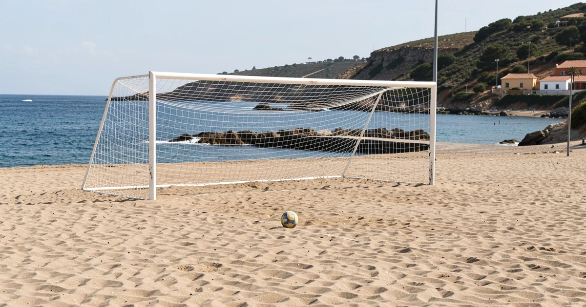Campo de fútbol playa vacío con porterías y balón en la arena