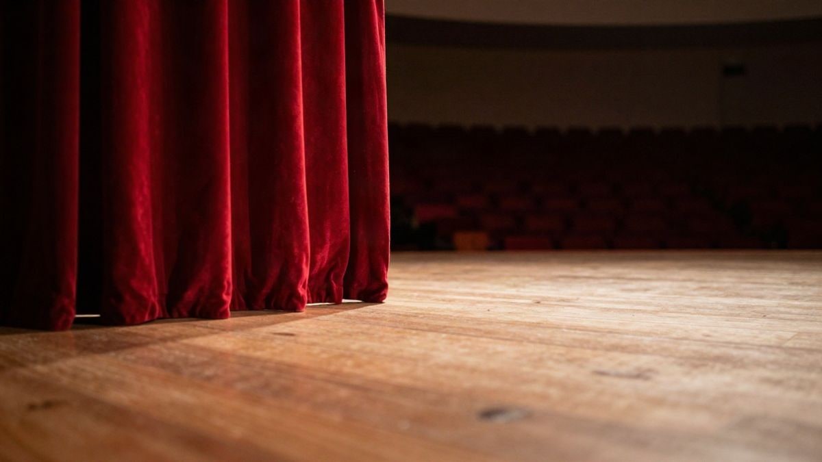 Imagen ilustrativa: escenario de teatro vacío con telón rojo y focos encendidos