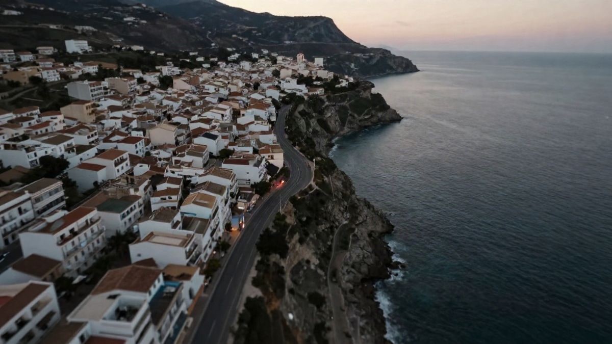 Imagen ilustrativa: vista cenital de un pueblo costero mediterráneo al atardecer, con carreteras y acantilados junto al mar.