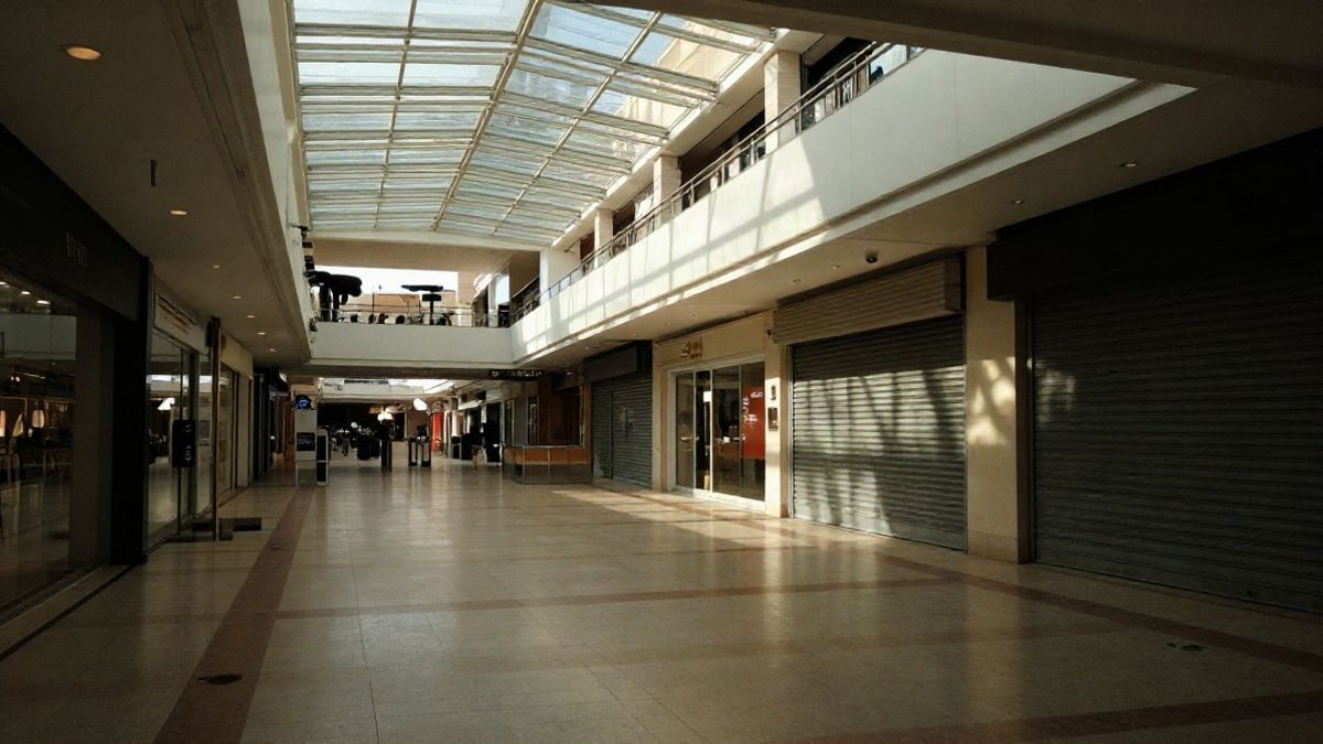Illustrative image: interior of an empty shopping centre with skylights and down metal blinds.