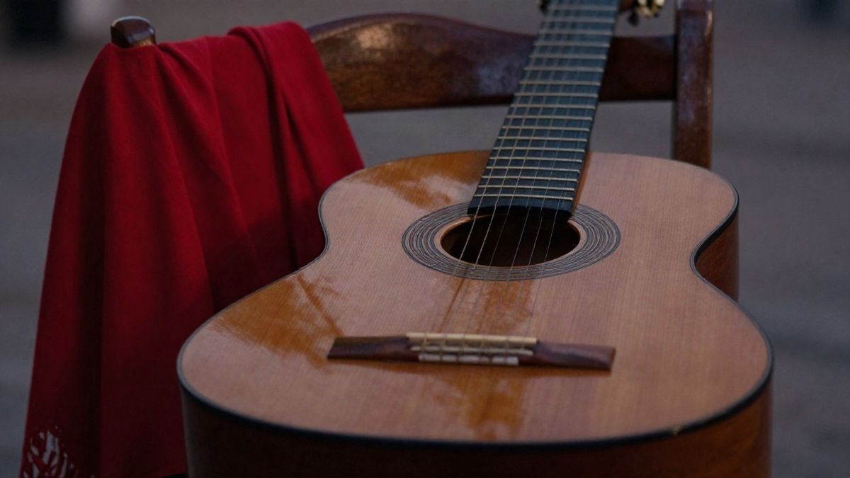 Imagen ilustrativa: una guitarra flamenca sobre una silla de madera con un chal rojo y un abanico, iluminada por la luz cálida del atardecer